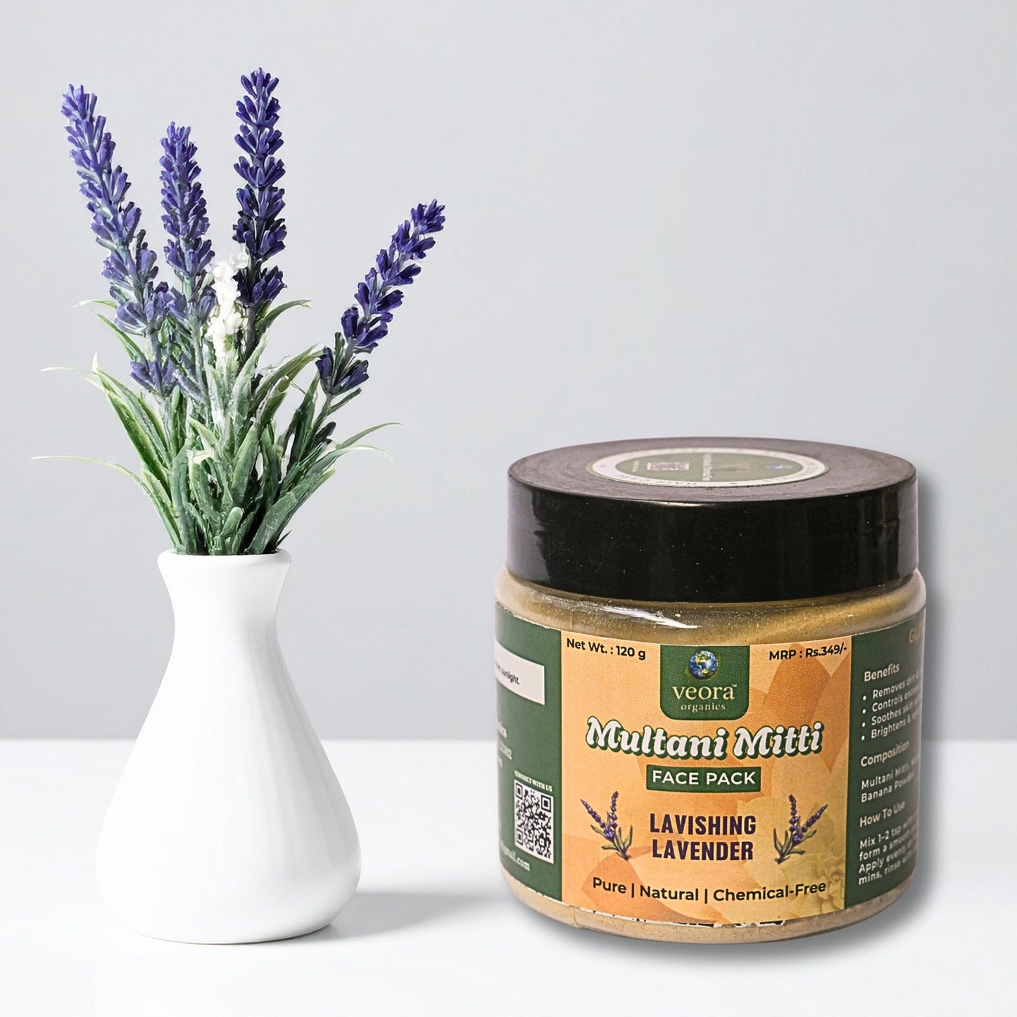 Jar of 'Multani Mitti' face pack with lavender flowers in a vase on a light gray background