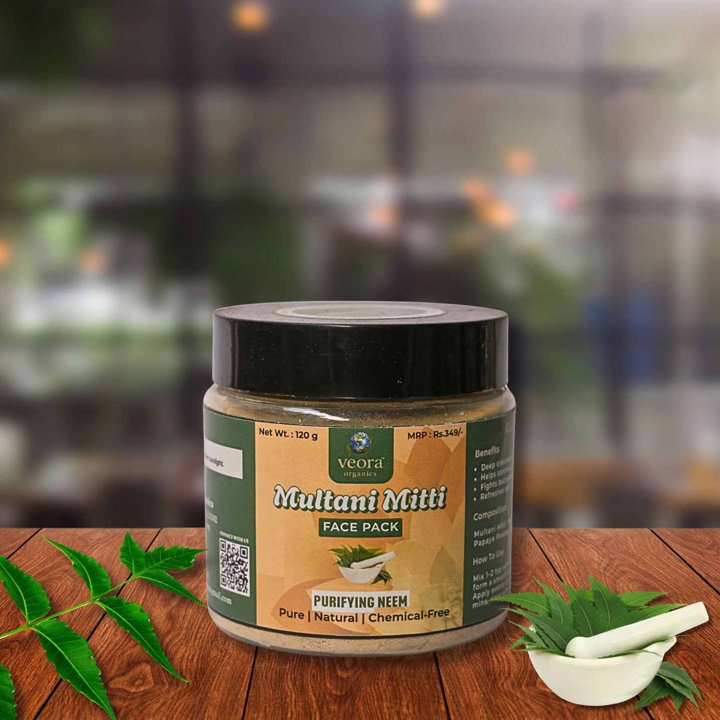 Jar of Multani Mitti face pack on a wooden table with green leaves and a pestle.