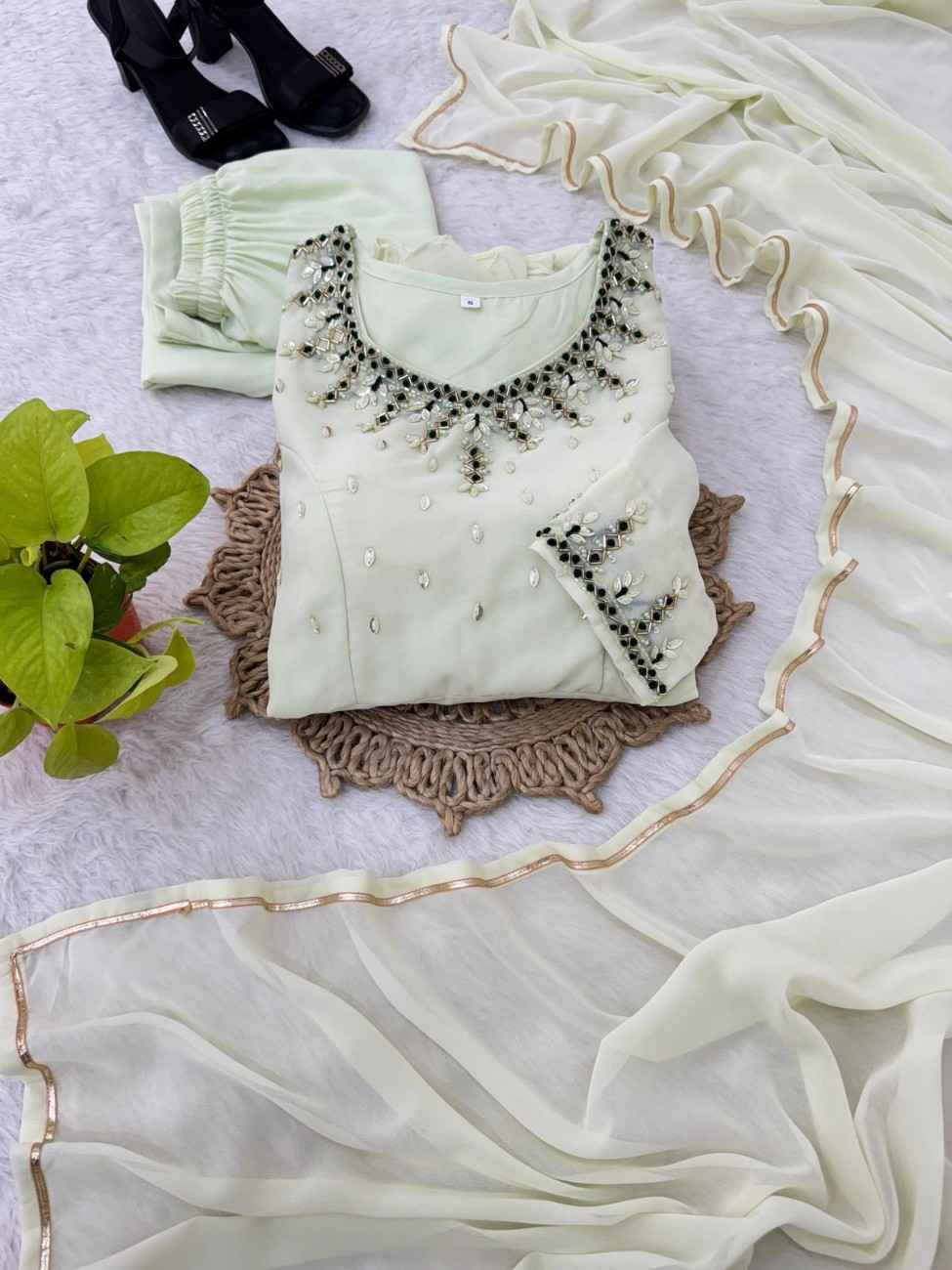 Light green blouse with black embellishments on a textured surface with a plant in the corner.