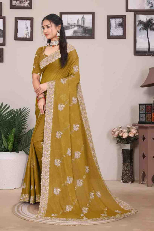 Woman wearing a mustard yellow saree with white patterns in a room with framed pictures on the wall.