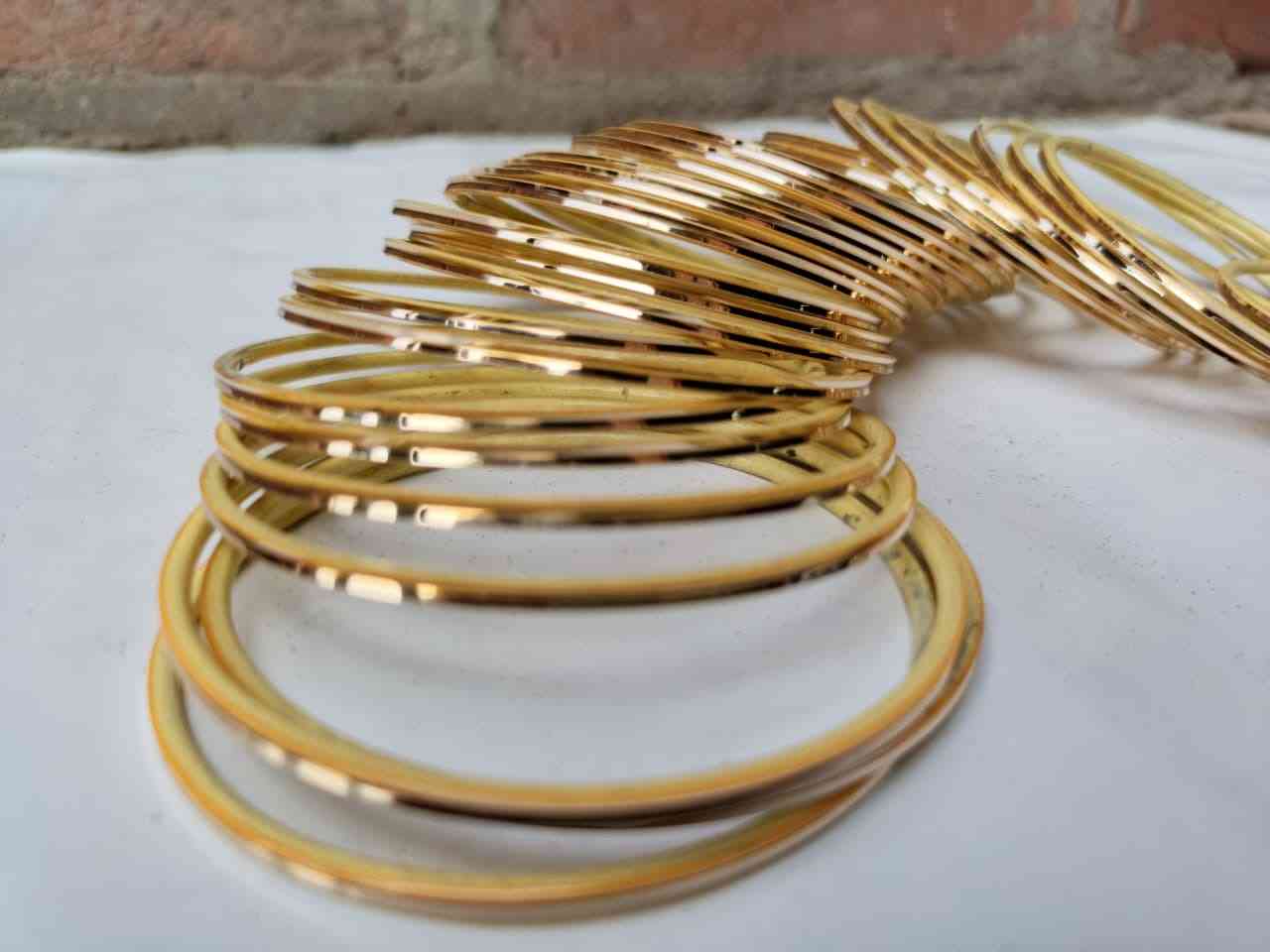 Gold bangles stacked on a white surface with a brick wall background