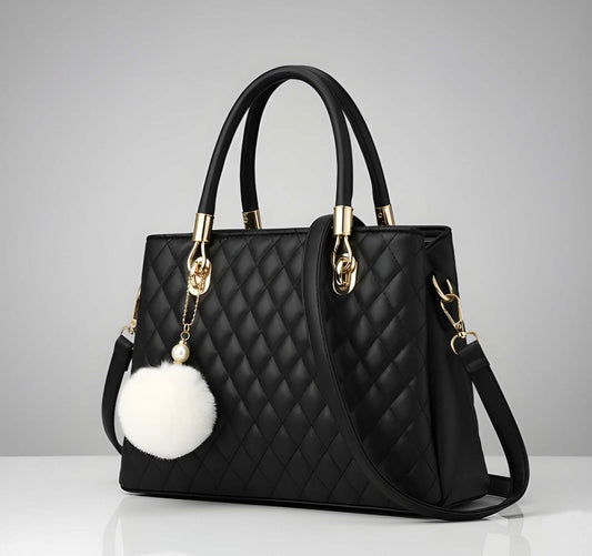 Black quilted handbag with gold accents and a white pom-pom on a gray background