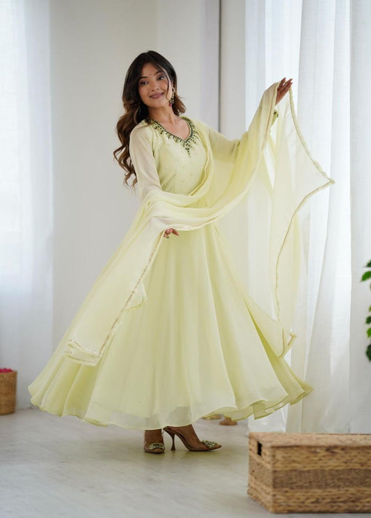 Woman in a light yellow traditional outfit with green embroidery standing in a bright room.