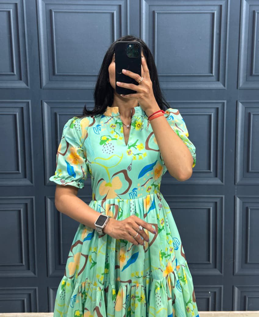 Person wearing a colorful dress with a floral pattern against a blue paneled wall.
