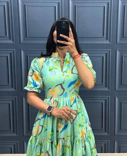 Person wearing a colorful dress with a floral pattern against a blue paneled wall.