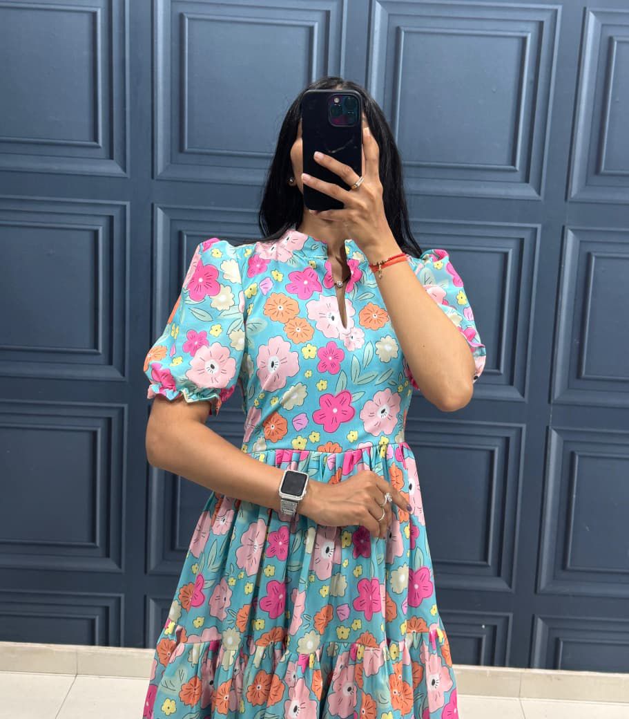 Person wearing a colorful floral dress in front of a blue paneled wall.