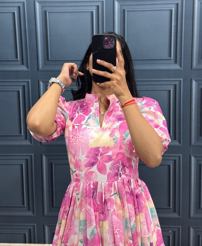 Person wearing a pink floral dress taking a mirror selfie against a blue paneled wall.