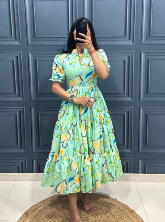 Person wearing a green floral dress taking a mirror selfie against a blue paneled wall.
