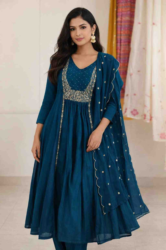 Woman wearing a teal traditional outfit with intricate designs indoors.