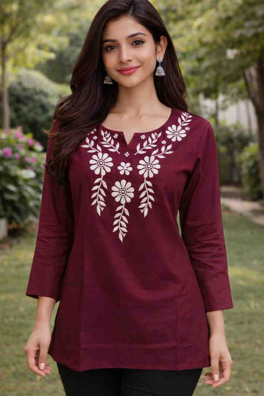 Woman wearing a maroon top with white floral embroidery outdoors.