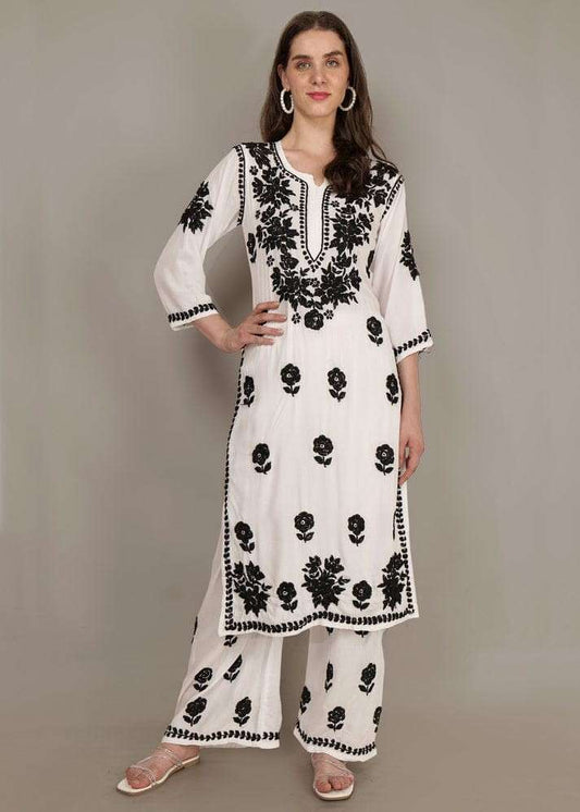 Woman wearing a white outfit with black floral embroidery against a gray background