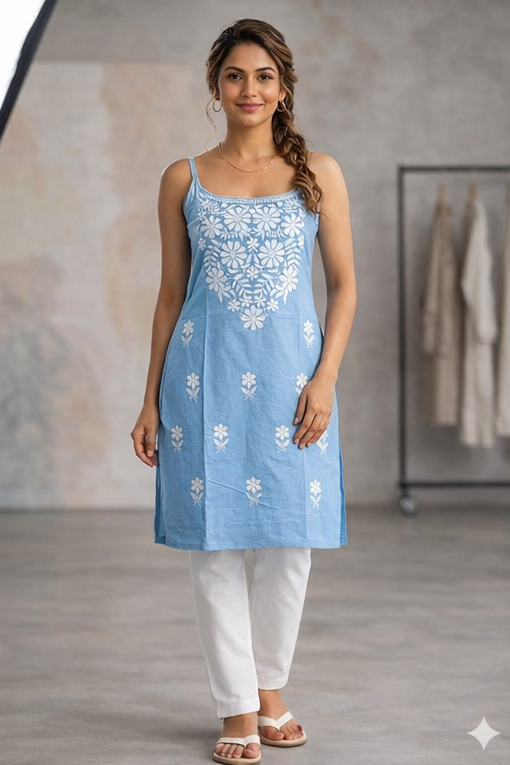 Woman wearing a blue embroidered dress with white pants in a neutral setting