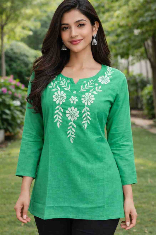 Woman wearing a green embroidered top in an outdoor setting